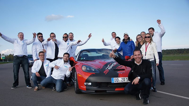 Ein Gruppenfoto vor einem roten Sportwagen beim PKW Fahrsicherheitstraining.