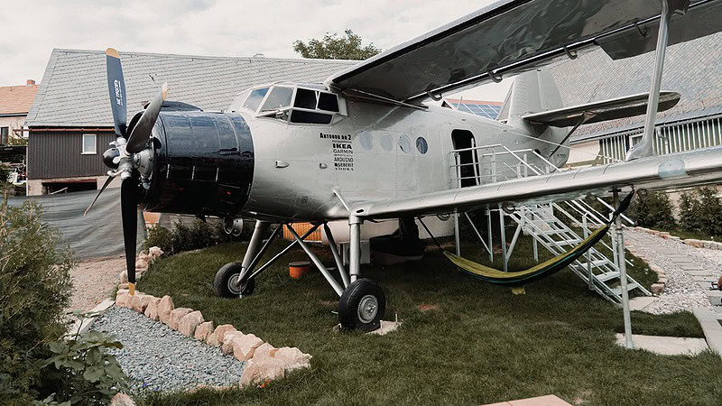 Seitliche Frontansicht einer Antonov AN-2 mit großem Doppeldeckerflügel und Propeller, die im Freien geparkt ist.