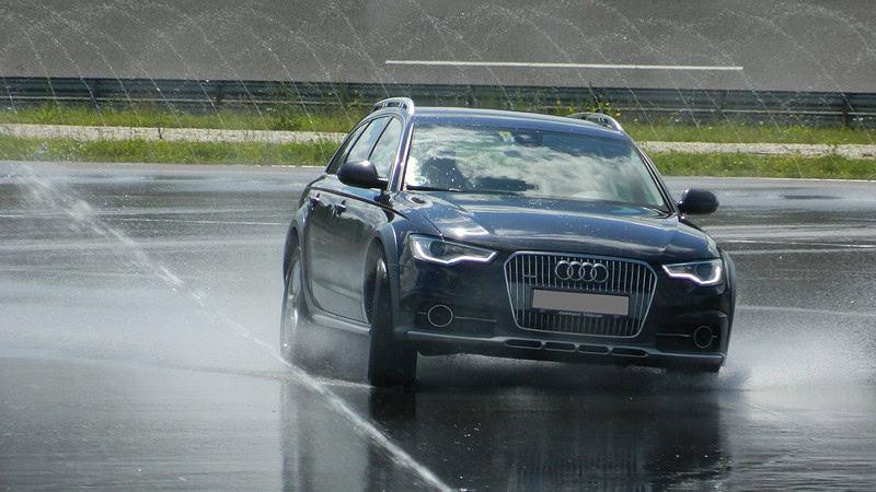 Ein Schwarzer Audi fährt beim Fahrsicherheitstraining auf einer nassen Fahrbahn.