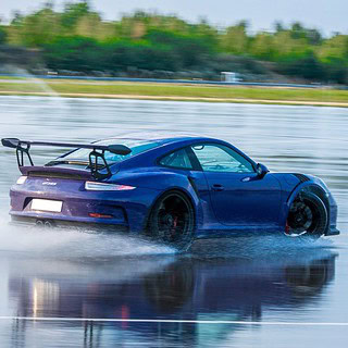 Ein bunter Porsche driftet auf einer nassen Fahrbahn.