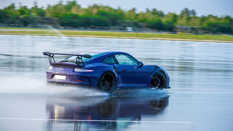 Ein bunter Porsche driftet auf einer nassen Fahrbahn.