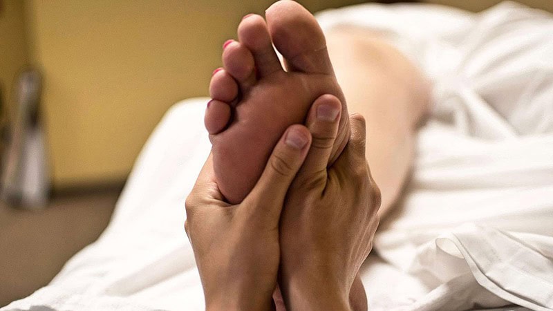 Ein Fuß wird bei einer Fußmassage von einem Masseur mit beiden Händen massiert.