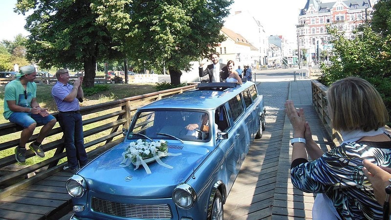 Ein frisch verheiratetes Paar schaut aus dem Dachfenster einer Trabant-Stretchlimousine.