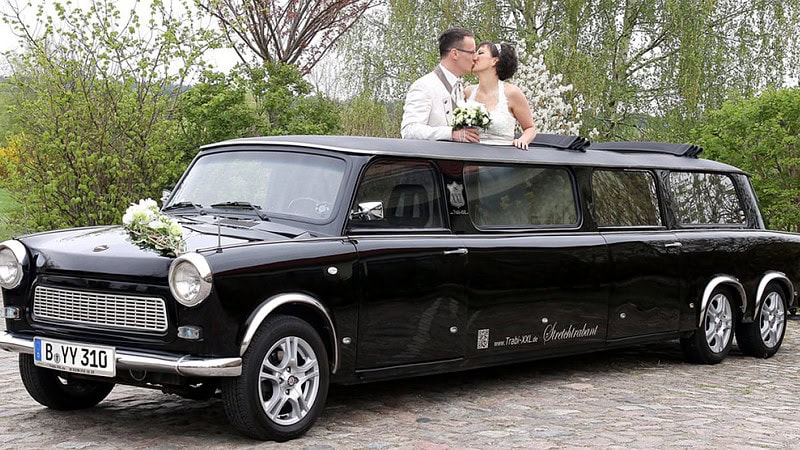 Ein Brautpaar küsst sich beim Blick aus dem Dachfenster einer Trabant-Stretchlimousine.