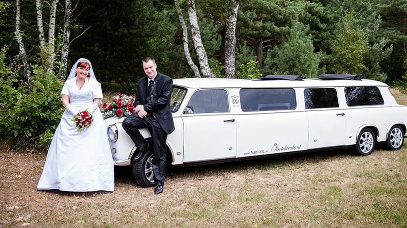 Ein Brautpaar vor einer geschmückten Trabant-Stretchlimousine.