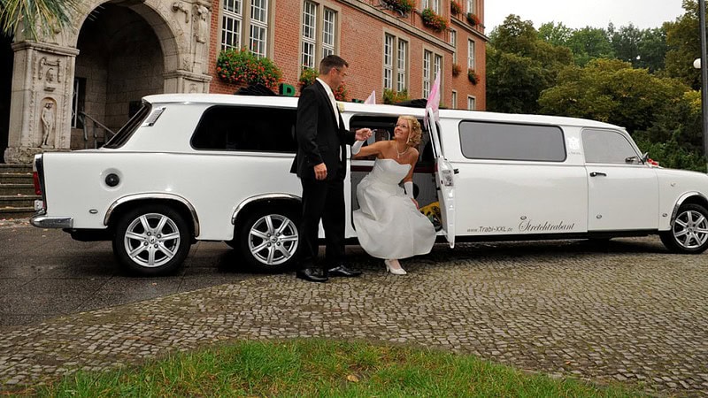 Ein Bräutigam hilft seiner Braut beim Aussteigen aus einer Trabant-Stretchlimousine.