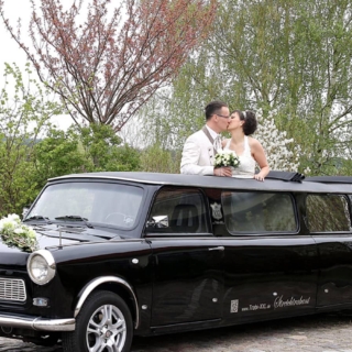 Brautpaar schaut aus dem Verdeck der Hochzeitstrabant-Stretchlimousine und küsst sich.
