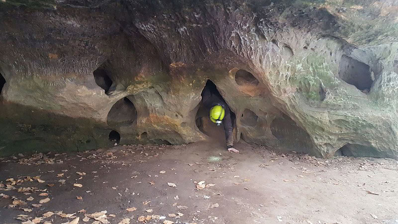 Ein Teilnehmer kriecht aus einem engen Loch heraus - Höhlenklettern in der Sächsischen Schweiz.