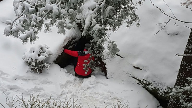 Eine Person versucht in eine Höhle zu gelangen. Um sie herum ist alles voller Schnee.