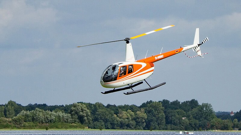 Ein kleiner weiß-orangener Hubschraube mit mehreren Person.