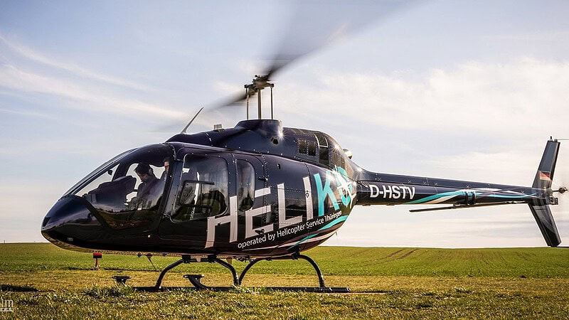 Hubschrauber steht auf einem Feld mit startenden Rotoren.