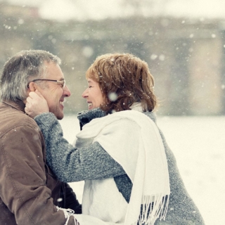 Ein alten Paar umarmt sich glücklich während es schneit, beim Lifestyle Fotoshooting