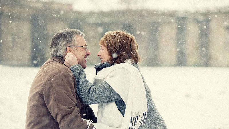 Ein alten Paar umarmt sich glücklich während es schneit, beim Lifestyle Fotoshooting