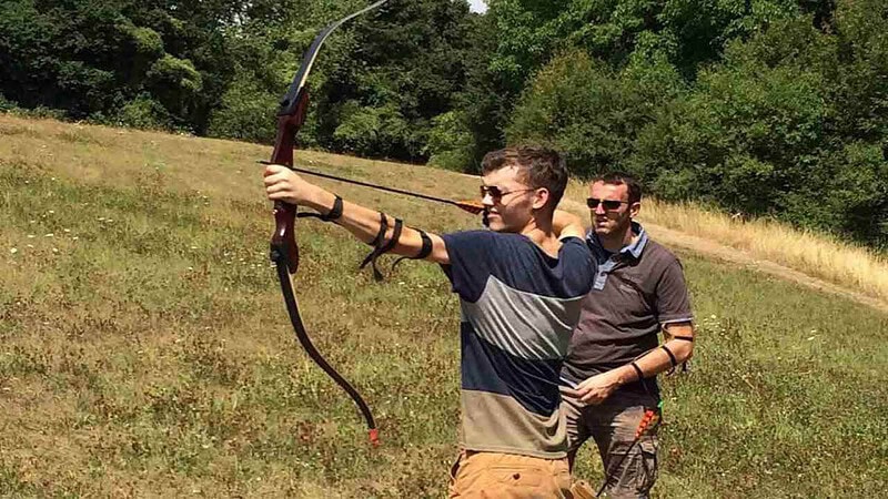 Ein Mann mit einem Trainer beim Bogenschießen in der Natur.