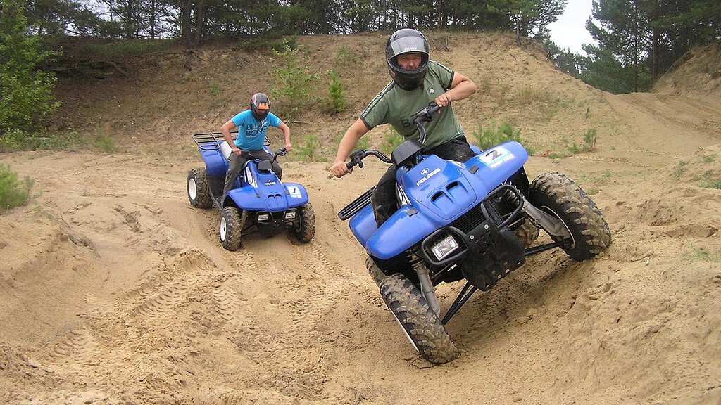 Zwei Männer fahren auf blauen Quads über sandiges Offroad Gelände.