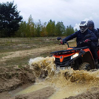 Ein Fahrer mit Beifahrer fahren mit einem Quad durch Matsch und Pfütze.