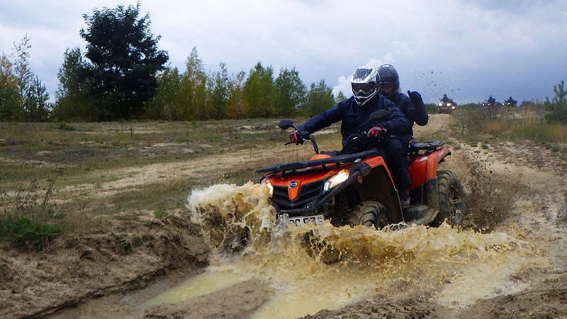 Ein Fahrer mit Beifahrer fahren mit einem Quad durch Matsch und Pfütze.