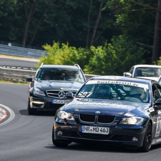 Sportwagen-Konvoi fährt mit hoher Geschwindigkeit über eine Rennstrecke, schwarzer BMW vorne im Fokus.