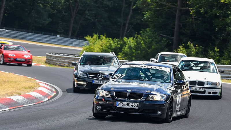 Sportwagen-Konvoi fährt mit hoher Geschwindigkeit über eine Rennstrecke, schwarzer BMW vorne im Fokus.