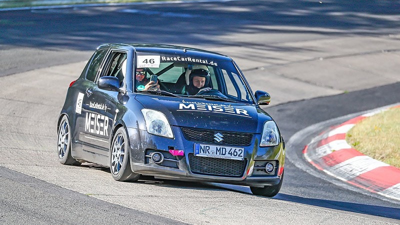 In einem kleinen Racecar fahren zwei Personen in eine Kurve auf einer Rennstrecke.