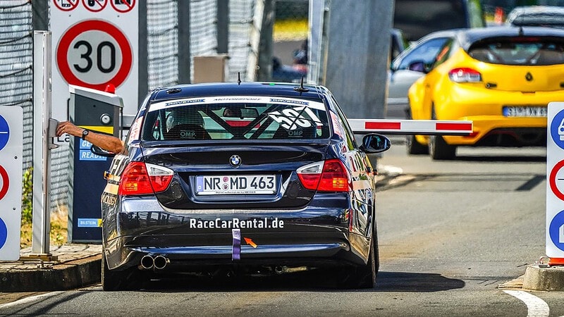 Ein Rennfahrer in einem BWM wartet vor eine Schranke darauf auf die Rennstrecke fahren zu dürfen.
