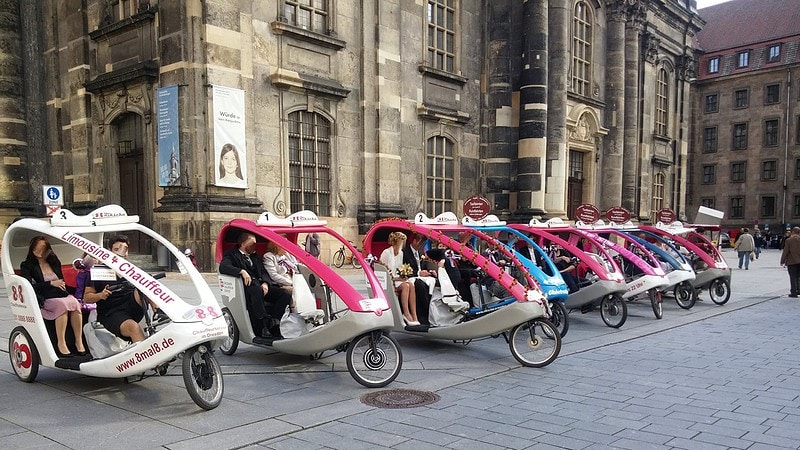 Acht Rikschas stehen nebeneinander in einer Reihe in Dresden bereit für eine Tour.