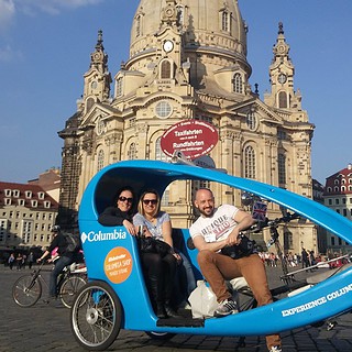 Pärchen sitzt in einer blauen Rikscha vor der barocken Frauenkirche in Dresden, Fahrer radelt durch die Stadt.