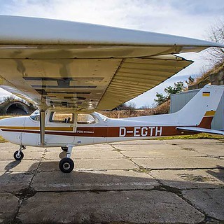 Kleine zweisitzige Maschine D-MVCS steht auf dem Flugplatz, rotes Dach und weiße Karosserie mit grünen Feldern dahinter.