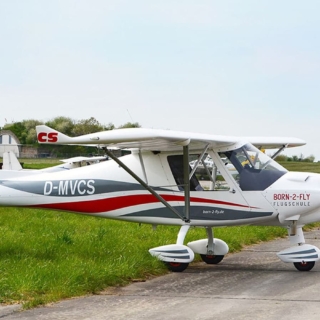 Kleines blaues Flugzeug startet in den Himmel, grüne Felder und Bäume im Hintergrund, Motorhaube glänzt.