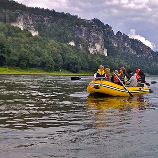 Zwei gelbe Schlauchboote mit mehreren Personen fahren auf der Elbe in der Sächsischen Schweiz entlang.