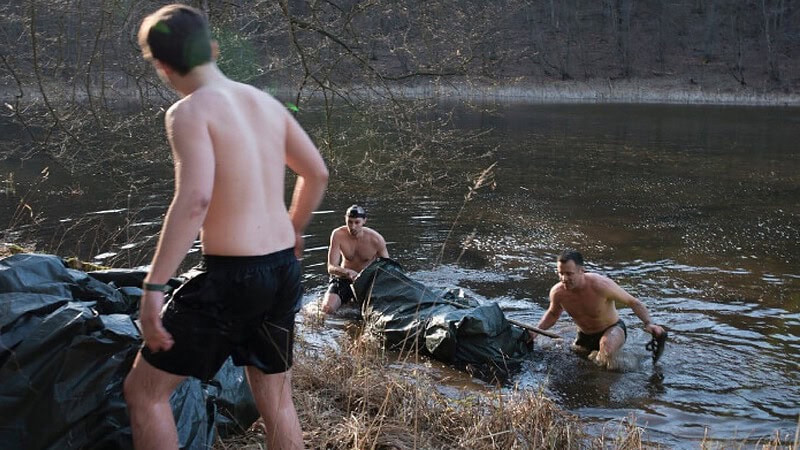 Drei Männer kommen mit einem selbst gebauten Floss aus einem Fluss bei einem Survival Wochenende.