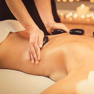 Vollkommene Entspannung bei Hot-Stone-Massage, glatte schwarze Steine liegen auf geöltem Rücken neben Kerzenlicht.