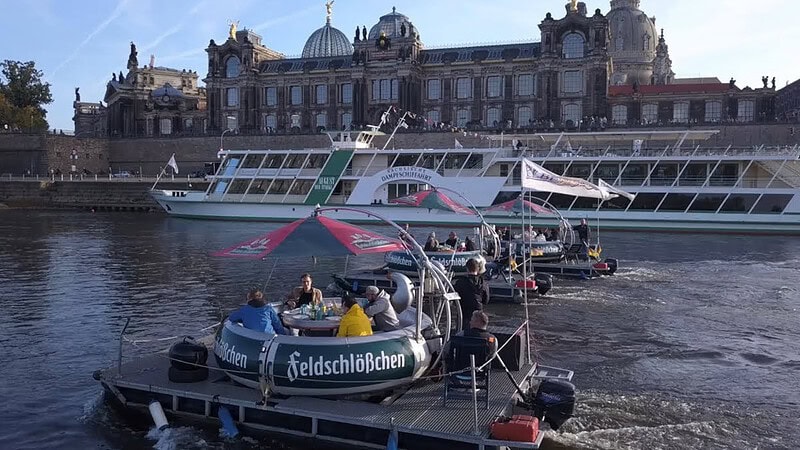 Drei Flöße fahren der Elbe entlang. Im Hintergrund ist das Terrassenufer der Dresdner Alt.