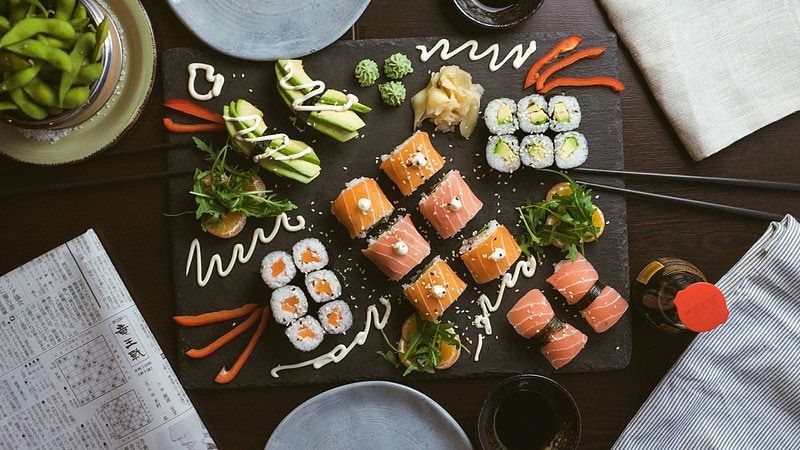 Vielfältige Sushi-Platte aus Lachs- und Gurkenrollen mit Sojasauce, Ingwer und Wasabi, kunstvoll angerichtet.