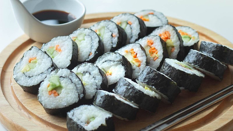 Ein Sushi Menü präsentiert auf einem Brett mit Sojasauce in einer kleinen Schale.
