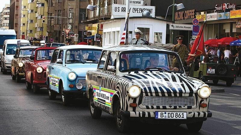 Kolonne bunter Trabant-Oldtimer mit Zebralackierung fährt auf einer Berliner Straße in einer Trabi-Safari.