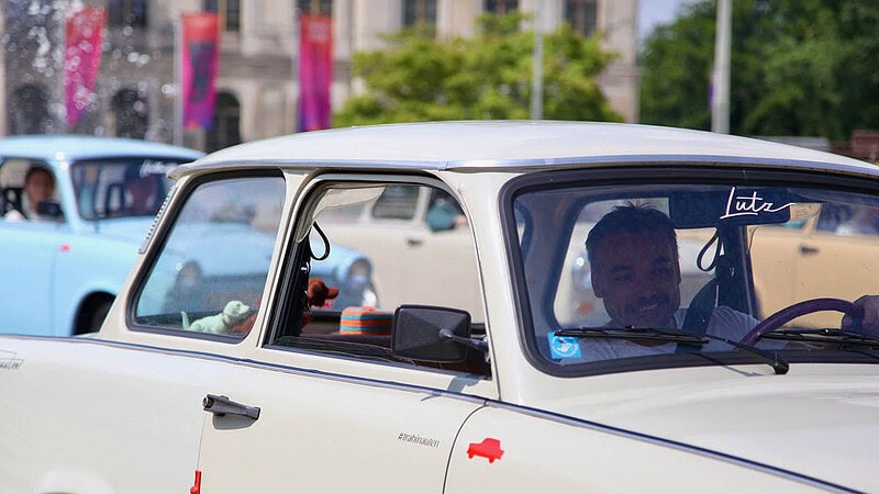 Blick auf einen Trabi mit einem Fahrer der glücklich lächelt.