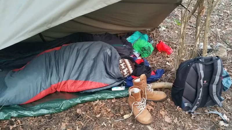 Ein Mann im Schlafsack mit Tarp als Schutz beim Survival Wochenende.