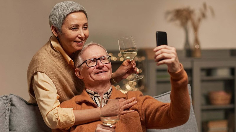Eine Ehepaar trinkt gemeinsam Weißwein redet mit jemandem auf einem Handy