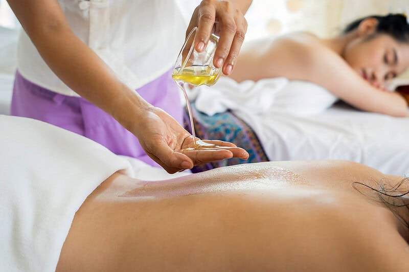 Eine Person gießt sich Massageöl in die Hand. Die anderen Personen auf dem Bild liegen wartend auf eine Massage auf dem Bauch.
