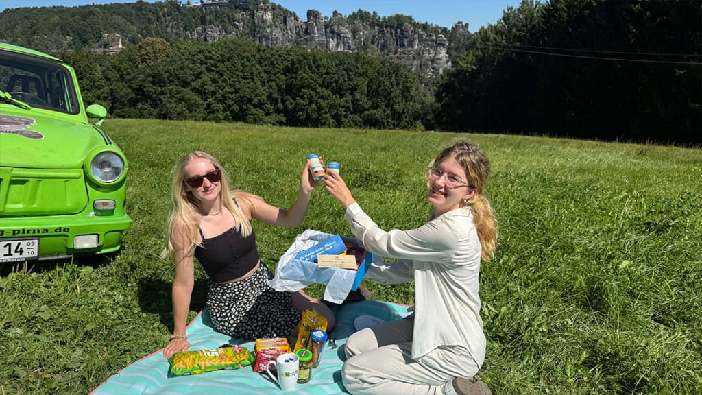 geschenkbox-trabi Zwei Frauen auf der Wiese beim Trabi Picknick packen die Geschenkbox für Trabant Erlebnisse aus
