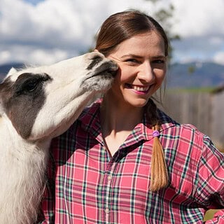 Ein Lama küsst eine Frau in einem karierten Hemd.