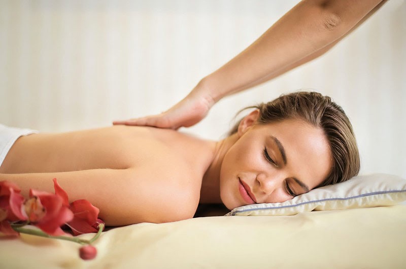 Eine Frau liegt auf dem Bauch mit verschlossenen Augen. Dabei erhält sie eine wohltuende Rückenmassage.