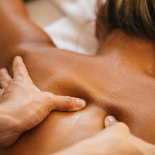 Therapeut lässt warmes Öl über den Rücken einer Frau laufen, Hände kneten die Muskeln in entspannter Spa-Atmosphäre.