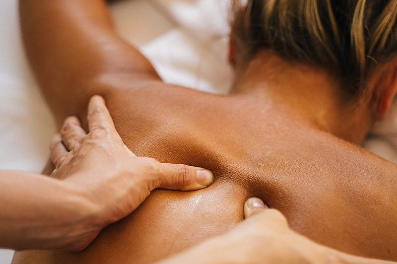 Therapeut lässt warmes Öl über den Rücken einer Frau laufen, Hände kneten die Muskeln in entspannter Spa-Atmosphäre.
