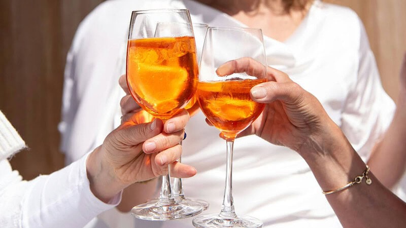 3 Personen in heller Kleidung stoßen mit einem Aperol an