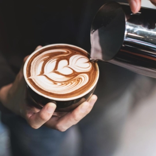 Barista gießt Milch in eine Tasse, um filigrane Latte-Art auf cremigem Cappuccino zu kreieren.