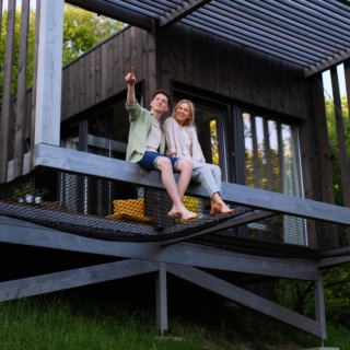Ein Paar sitzt zusammen auf einer Terrasse eines Tiny Houses, wo sie übernachten werden