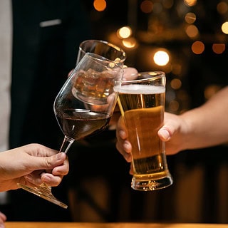 Zwei Menschen stoßen mit Weinglas und Bierglas in einer gemütlichen Bar bei warmem Licht an.