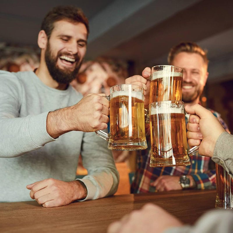 Fröhliche Männer stoßen in einer Bar mit großen Bierkrügen an und genießen gemeinsam den Abend.